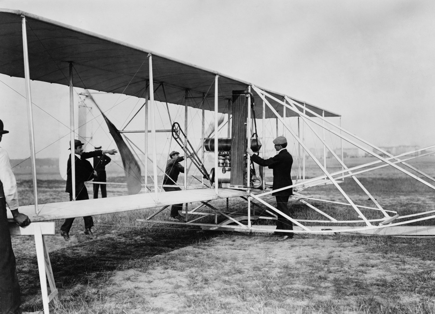 Orville Wright with his airplane in Berlin, Germany, at Tempelhof Field, 1909. Orville stands near the engine, as two men turn the propellers to start the engine  (BSLOC_2018_2_151)